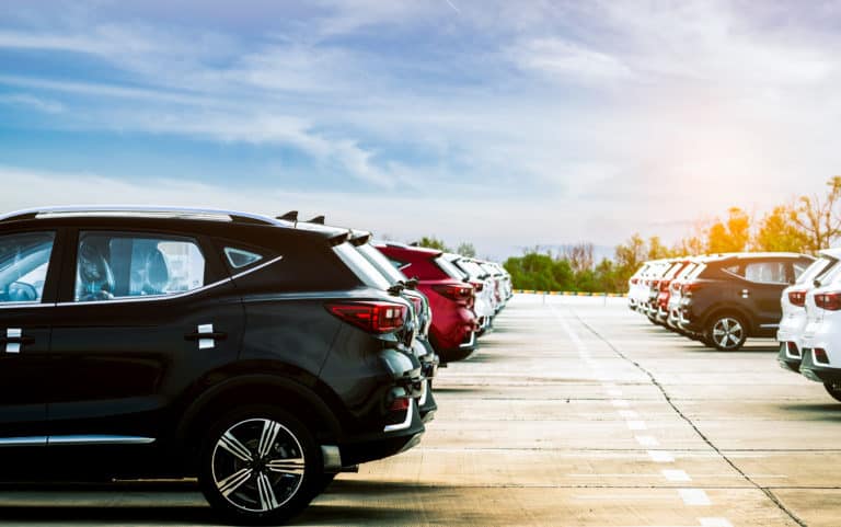 Luxury black, white and red new suv car parked on concrete parking area at factory with blue sky and clouds. Car stock for sale. Car factory parking lot. Automotive Industry concept. Car dealership.